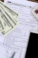 Composition of items lying on the 1040 tax form. Dollar bills, pen, calculator, smartphone, paper clip and notepad. The time to pay taxes photo