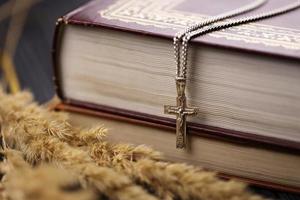 Silver necklace with crucifix cross on christian holy bible book on black wooden table. Asking blessings from God with the power of holiness photo