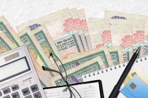Billetes de 1000 rupias de Sri Lanka y calculadora con gafas y bolígrafo. concepto de pago de impuestos o soluciones de inversión. planificación financiera o papeleo contable foto