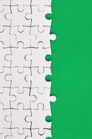 Fragment of a folded white jigsaw puzzle on the background of a green plastic surface. Texture photo with copy space for text