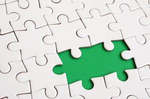 Close-up texture of a white jigsaw puzzle in assembled state with missing elements forming a green pad for text. Copy space photo