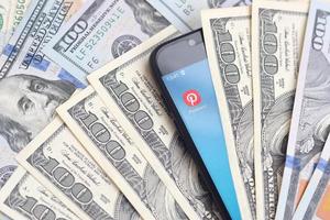 KHARKOV, UKRAINE - JULY 2, 2021 Smartphone screen with Pinterest app and lot of hundred dollar bills. Business and social networking concept photo