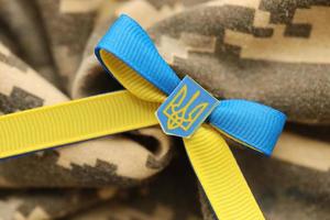 TERNOPIL, UKRAINE - SEPTEMBER 2, 2022 Ribbon with Ukrainian Coat of Arms and national flag colors on army camouflage uniform photo