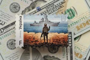 TERNOPIL, UKRAINE - SEPTEMBER 2, 2022 Famous Ukrainian postmark with russian warship and ukrainian soldier as wooden souvenir on big amount of US dollar bills photo