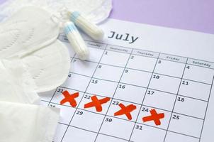 Menstrual pads and tampons on menstruation period calendar with red cross marks lies on lilac background photo