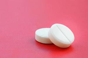 A few white tablets lie on a bright red background surface. Background image on medical and pharmaceutical topics photo