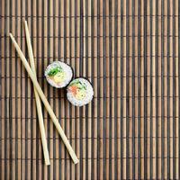 Sushi rolls and wooden chopsticks lie on a bamboo straw serwing mat. Traditional Asian food. Top view. Flat lay minimalism shot with copy space photo