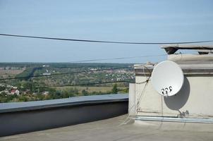 antena parabólica blanca con tres convertidores montados en un muro de hormigón en la azotea de un edificio residencial. televisión via satélite foto