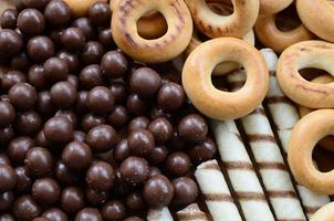 A lot of crispy sweet tubules, chocolate melting balls and yellow bagels lie on a wooden surface. Close up view photo