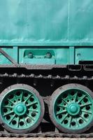 Side view of the vehicle on a caterpillar track with black tracks and green wheels and a side metal wall