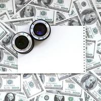 dos lentes fotográficos y un cuaderno blanco se encuentran en el fondo de muchos billetes de dólar. espacio para texto foto