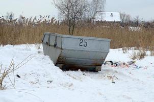 Trash bin at the side of street in winter with lip garbage container winter snow. Metal container for household waste photo