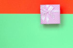 Small pink gift box lie on texture background of fashion pastel turquoise and red colors paper photo