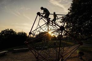 siluetas de niños juegan en la escalada de poliedro de cuerda en el patio de recreo al aire libre. foto