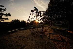 Silhouettes of children play in rope polyhedron climb at playground outdoor. photo