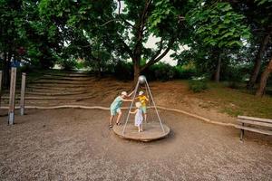 tres niños montan en el patio de recreo. centrífuga, columpio para niños. foto