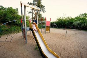 Baby girl slides in children's playground toy set in public park. photo