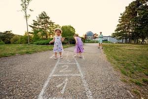 Two sisters playing hopscotch in park. Kids game, children outdoor activities. photo