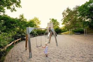 Baby girl swing in children's playground toy set in public park. photo