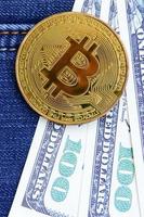 Golden Bitcoin and dollar bills lies on a blue jeans fabric. New virtual money. New crypto currency in the form of the coins photo