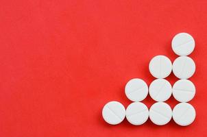 Several white tablets lie on a bright red background in the form of a triangular arrow. Background image on medicine and pharmaceutical topics photo