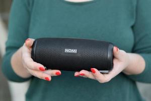 KHARKOV, UKRAINE - JULY 2, 2021 Young girl holds Nomi black portable USB speaker by Nomi electronics company. New Outstanding Mobile Ideas