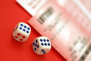 Red lottery ticket with dice lies on pink gambling sheets with numbers for marking to play lottery. Lottery playing concept or gambling addiction. Close up photo
