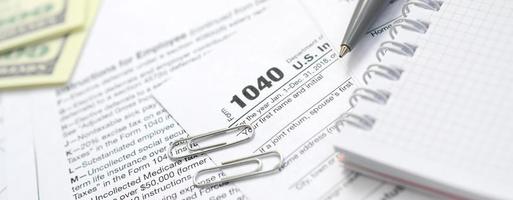 The pen, notebook and dollar bills is lies on the tax form 1040 U.S. Individual Income Tax Return. The time to pay taxes photo