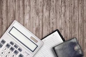 Office flat lay composition with calculator, address book and black purse on brown wooden table background with top view. Accountant paperwork concept photo