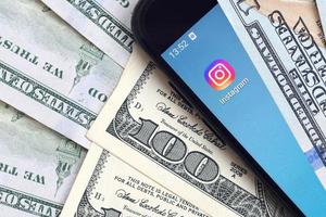 KHARKIV, UKRAINE - MAY 4, 2020 Smartphone screen with Instagram app and lot of hundred dollar bills. Business and social networking concept photo