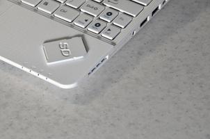 A compact SD memory card lies on a white netbook. The digital information storage device is ready for use. Concept of modern technologies photo