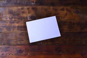 Photo of a clean white blank sheet of paper lie on a brown wooden background. Plenty of space for text