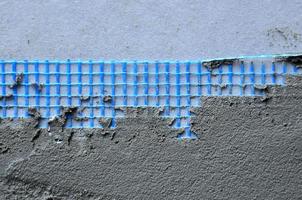 The texture of the wall, covered with gray foam polystyrene plates, covered with a blue reinforcing mesh and covered with a mixture for gluing it. Stage of wall insulation photo