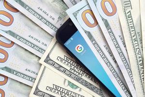 KHARKOV, UKRAINE - JULY 2, 2021 Smartphone screen with Google app and lot of hundred dollar bills. Business and social networking concept photo