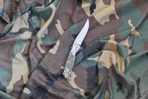 Military knife on army camouflage clothes close up. Background with copy space for military or special service design photo