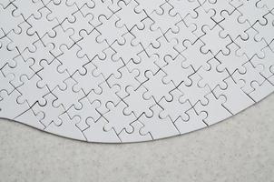 A white jigsaw puzzle in the complete form lies on a treated stone surface. Textured image with copy space photo