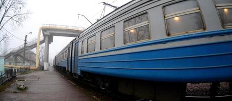 The railway track in a misty morning. The Ukrainian suburban train is at the passenger station. Fisheye photo with increased distortion