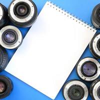 Several photographic lenses and white notebook lie on a bright blue background. Space for text photo