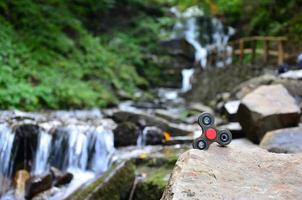 The wooden spinner lies on the rocks against the background of a small waterfall and a river photo