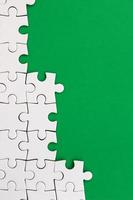 Fragment of a folded white jigsaw puzzle on the background of a green plastic surface. Texture photo with copy space for text
