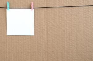 White blank card on rope on a brown cardboard background. Creative reminder, small sheet of paper on wooden clothespin, memo backdrop photo