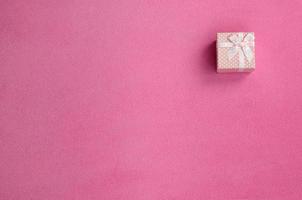 A small gift box in pink with a small bow lies on a blanket of soft and furry light pink fleece fabric. Packing for a gift to your lovely girlfriend photo