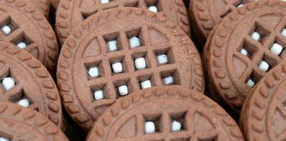 Detailed picture of dark brown round sandwich cookies with coconut filling close up. Background image of several treats for tea photo