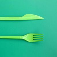 Disposable plastic cutlery green. Plastic fork and knife lie on a green background surface photo