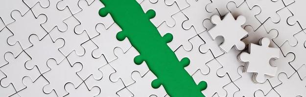 The green path is laid on the platform of a white folded jigsaw puzzle. The missing elements of the puzzle are stacked nearby. Texture image with space for text photo