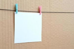 White blank card on rope on a brown cardboard background. Creative reminder, small sheet of paper on wooden clothespin, memo backdrop photo