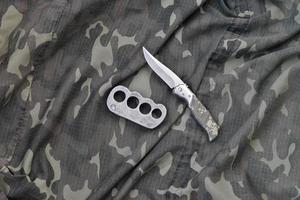 cuchillo y nudillos de latón sobre un fondo de ropa de camuflaje. herramientas para la autodefensa o ataques de delincuentes foto