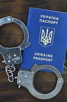 A Ukrainian passport with police handcuffs lies on a wooden table. Problems with the law during the crossing of the borders of countries. The illegal side of visa-free travel for Ukrainian citizens photo