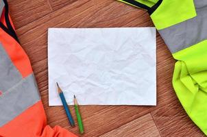 A crumpled sheet of paper with two pencils surrounded by green and orange working uniforms photo