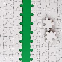 The green path is laid on the platform of a white folded jigsaw puzzle. The missing elements of the puzzle are stacked nearby. Texture image with space for text photo